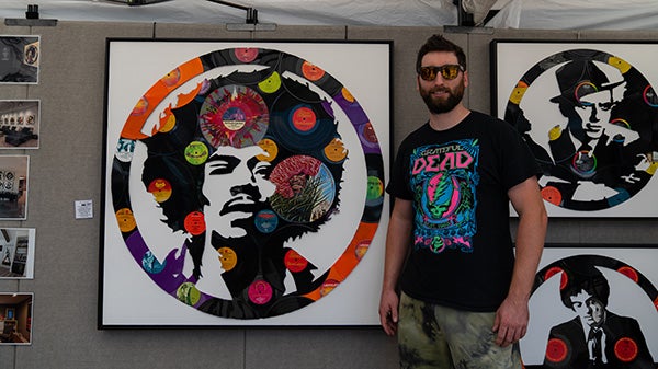 Alex Grimmer, an artist who creates images of music artists and album covers using vinyl records, stands next to his large piece of Jimi Hendrix.