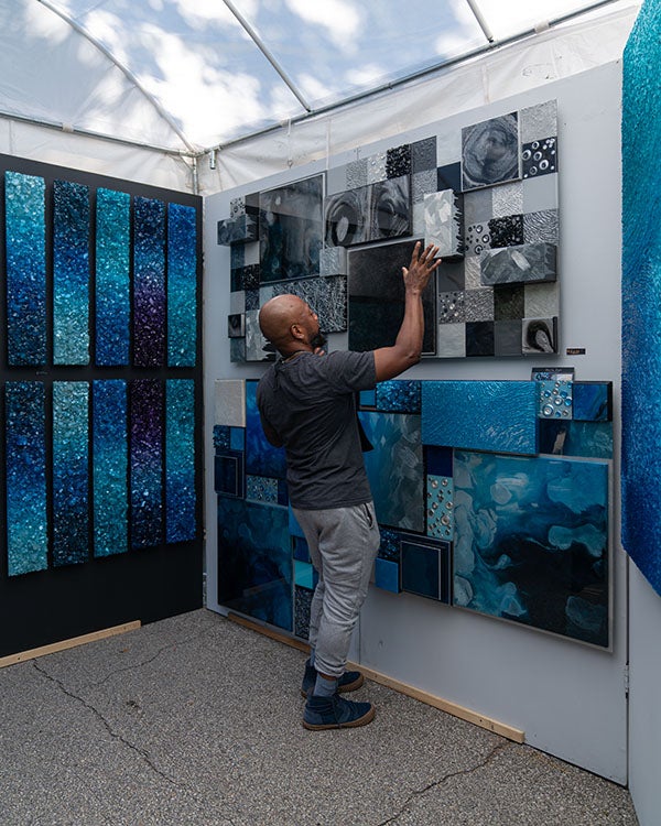 The artist, Neil Russell, a black man, faces his artwork and points as he explains more about what inspired his art, which is made from fragments of glass and resin.