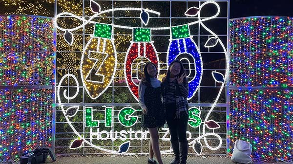 Grace, a Rice student, poses with Sarah, a Rice alumna, in front of a lit-up sign that says "Zoo Lights Houston Zoo."