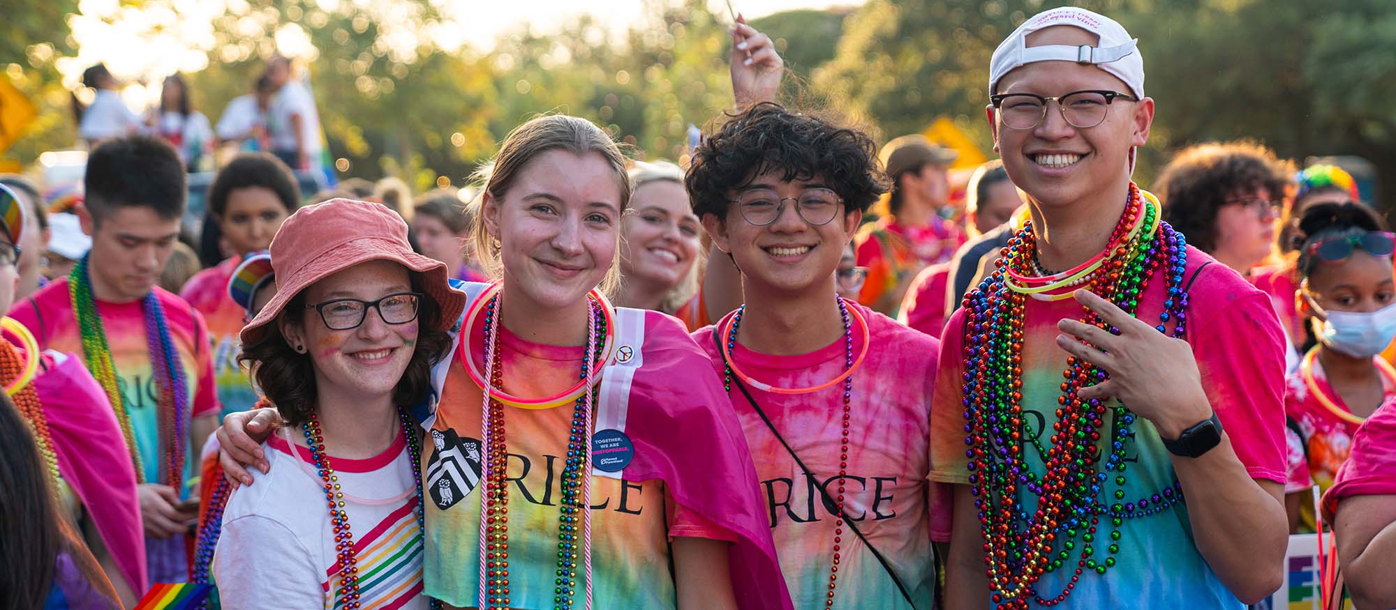 A group of Rice students wearing rainbow tie-dyed shirts, beads and glow necklaces smile for a picture at Houston's Pride Parade in 2022.