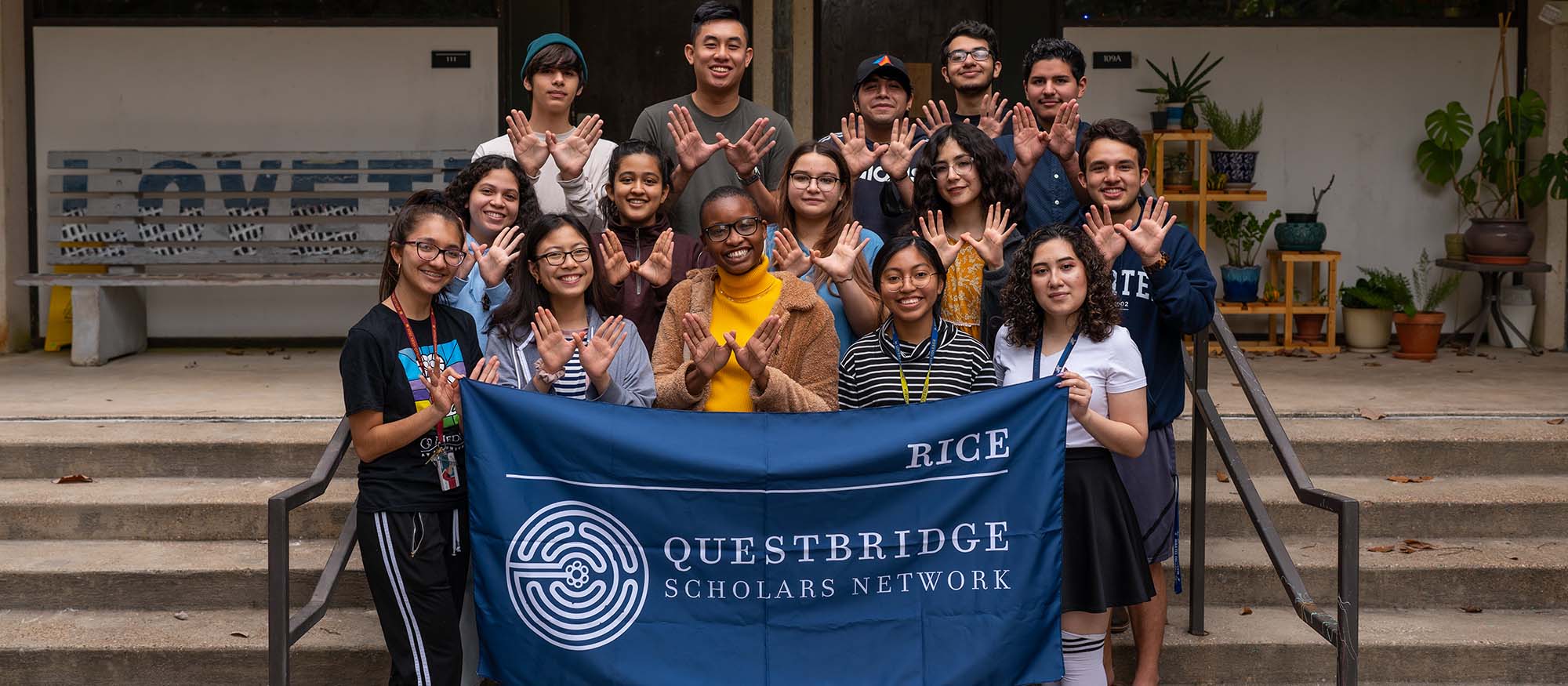 A group of students that are apart of the Questbridge Scholars Network pose and smile for a picture while holding a flag that says "Questbridge Scholars Network."