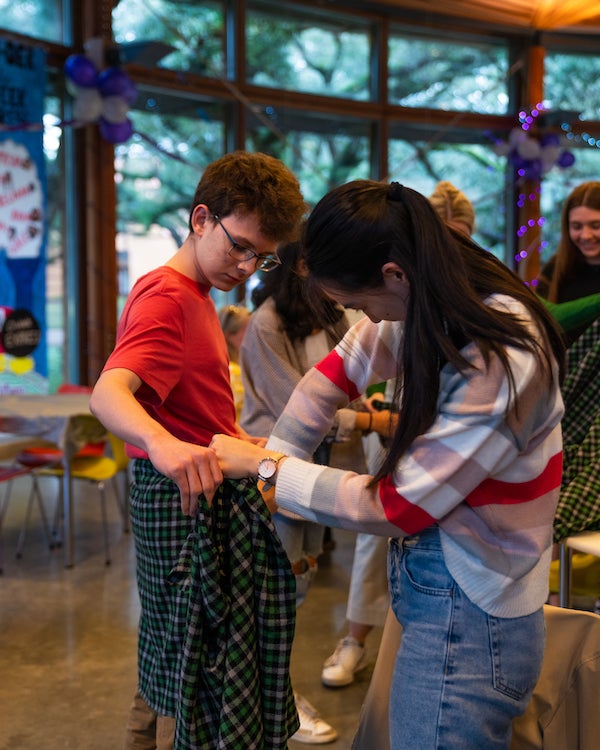 One student helping another student tie a kilt around their waist.