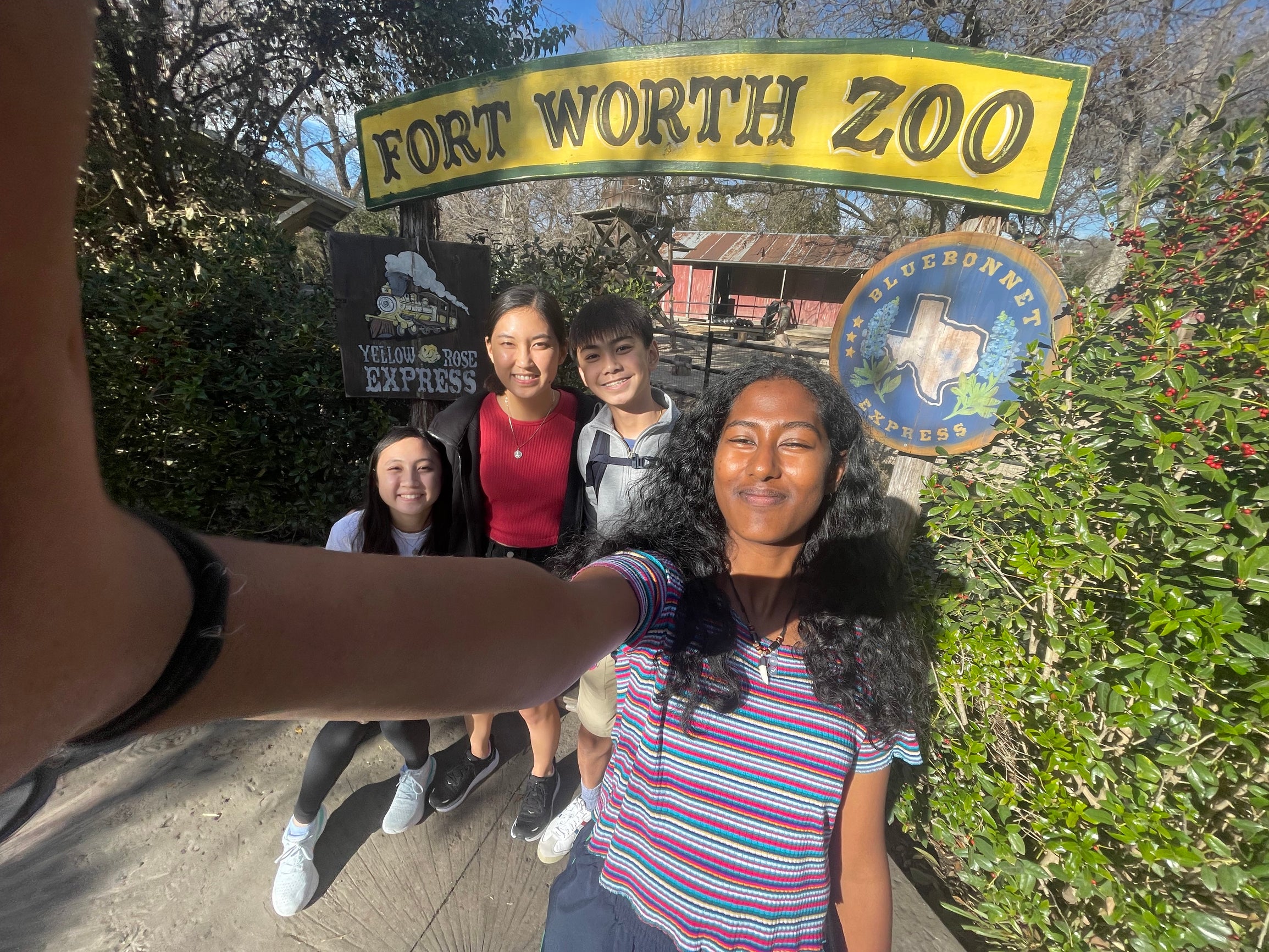 A selfie taken by one person with four people in frame and a "Fort Worth Zoo" sign behind them.