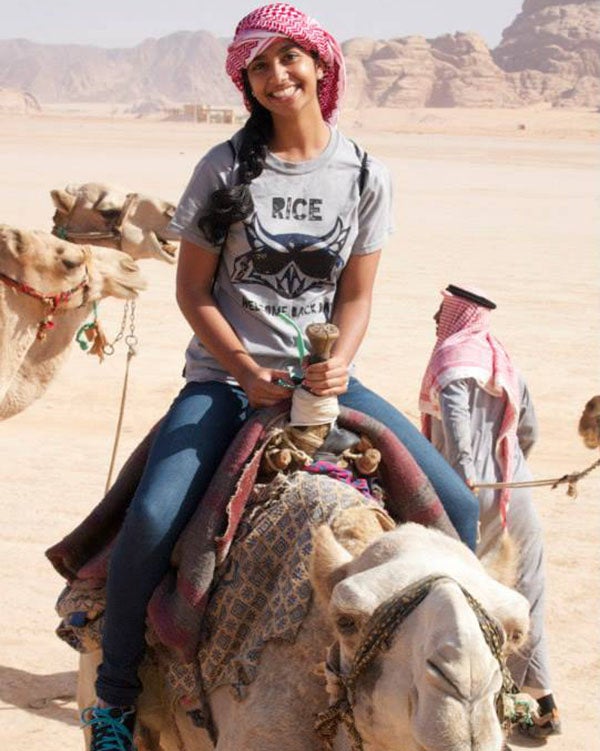 Sneha is wearing a Rice t-shirt and riding on a camel in the Wadi Rum Desert.