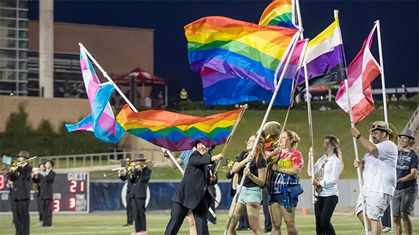 Students from the Rice Marching Owl Band wave LGBTQIA+ flags on the Rice football field to celebrate Pride.