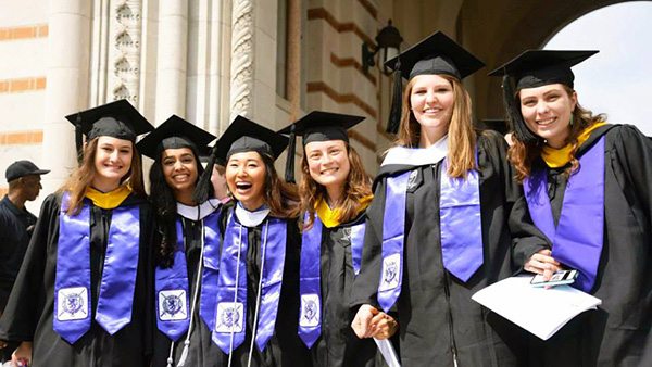 A group of women, including Sneha, stand in front of the Sallyport Arch in their cap and gowns after graduating from Rice.