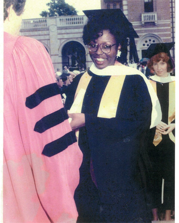 Tamara, in her cap and gown, smiles at the camera and receives her diploma as she graduates.