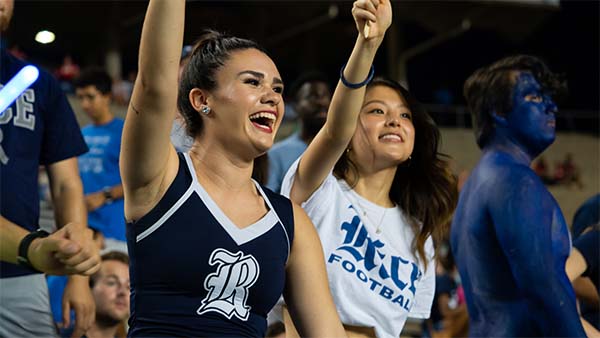 A member of the Rice dance team and a Rice fan are both raising their left arms next to each other to cheer on the players.