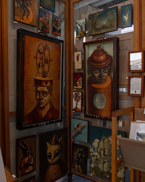 A picture of artist Jay Long's booth with a variety of pieces of his work. His work is surreal portraits that are mixed media oil paint over collaged text from found books.
