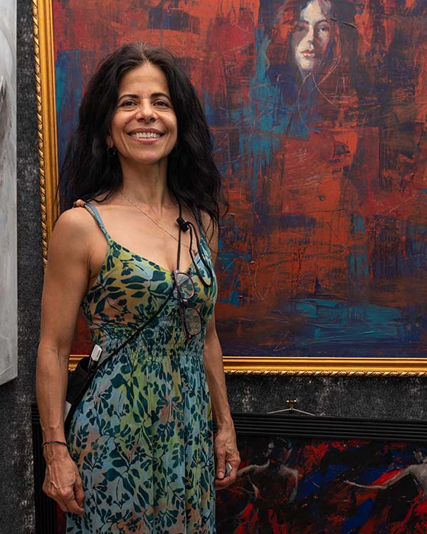 Hilda Rueda, an artist, smiles and poses in front of one of her pieces of art.