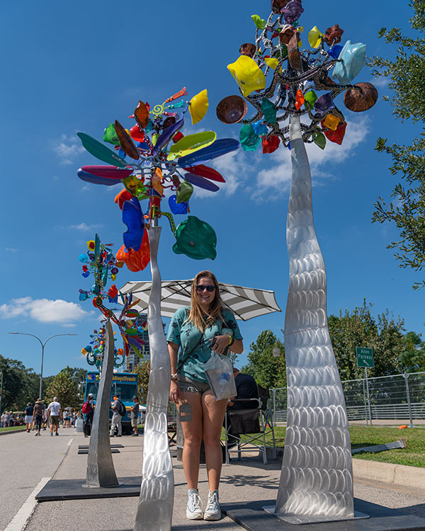 Rice student Julie poses next to two pieces of outdoor art made of metal that look like flowers and are taller than her (approximately 7-8 ft high).