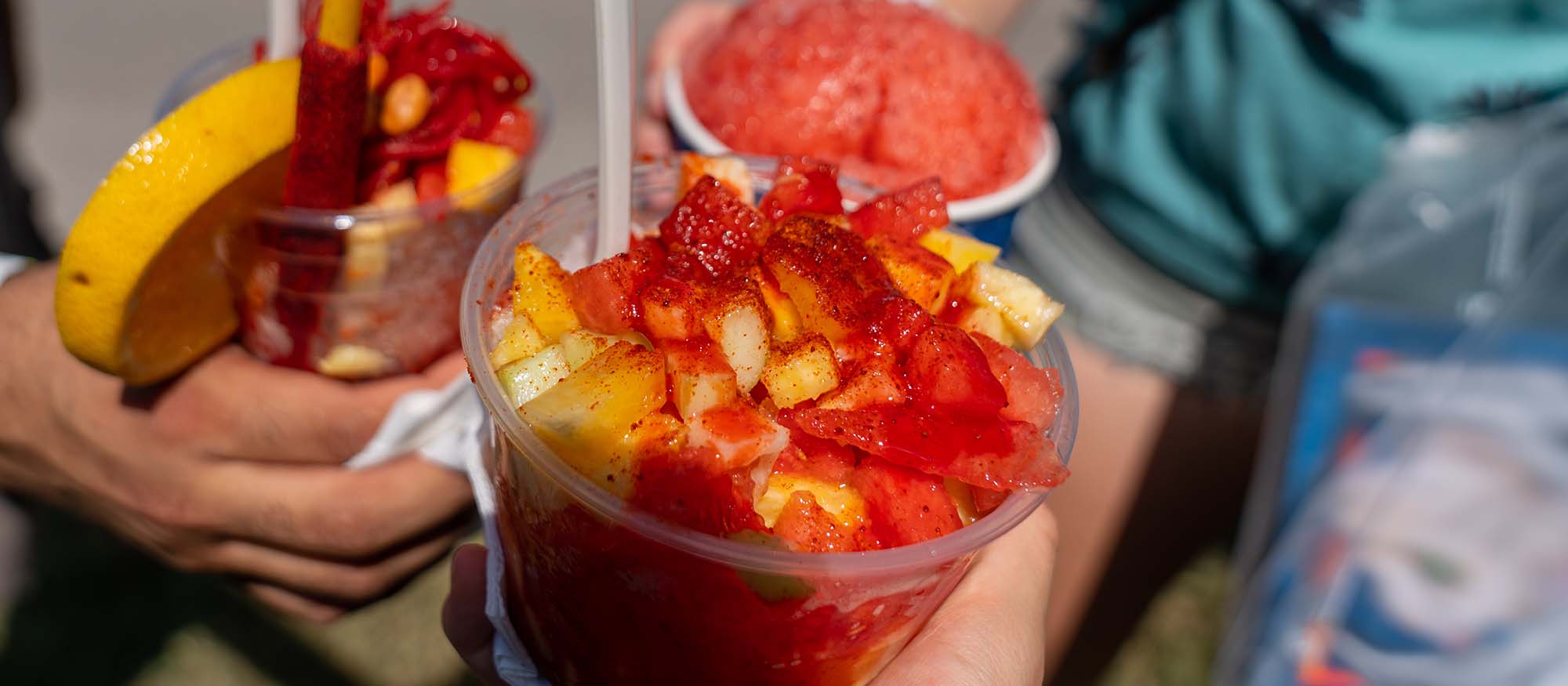 Close up picture of a strawberry snow cone and two different types of mangonadas.