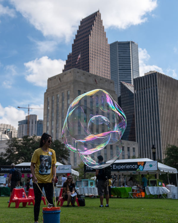 A young volunteer for the art festival uses sticks and rope to create a huge bubble in front of the backdrop of the buildings in downtown Houston.