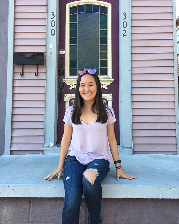 Isabel smiles as she sits on a porch in front of a red door with gold accents.