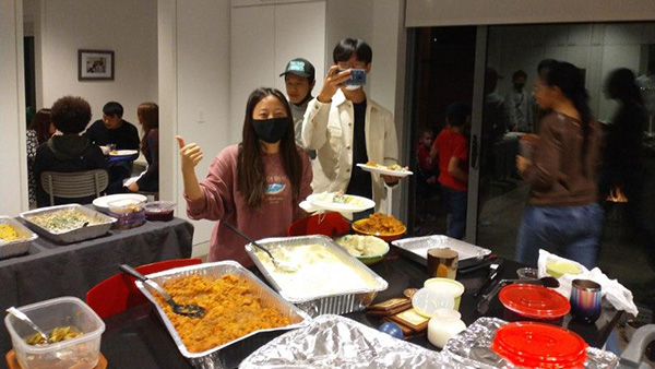 Two Rice students wearing masks pose for a picture in front of one of the tables filled with food.
