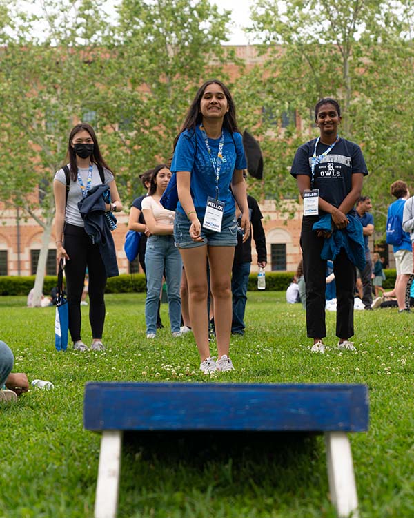 A picture taken from behind a bean bag toss board, with a female admitted student tossing a bean bag towards the board and the camera.