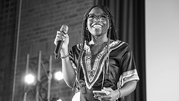 A Black student holding a microphone smiles as she performs at Africayé 
