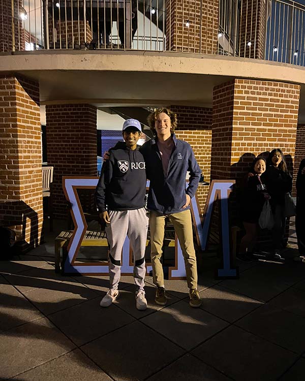 Two male students from Martel College stand in front of the large Greek letters that represent Martel College - Sigma Pi Mu.