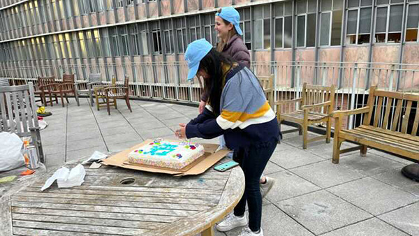 Two female students from Martel College stand facing Martel's annual birthday cake in order to cut it up and pass it out.