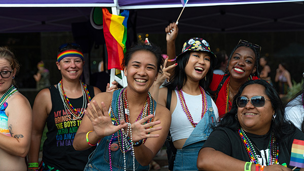 A group of students at the Houston Pride Parade smile while one student does the Rice Owls sign with her hand.