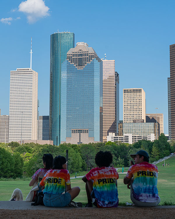 Three students from Rice sit facing away from the camera with the Houston skyline in the background.