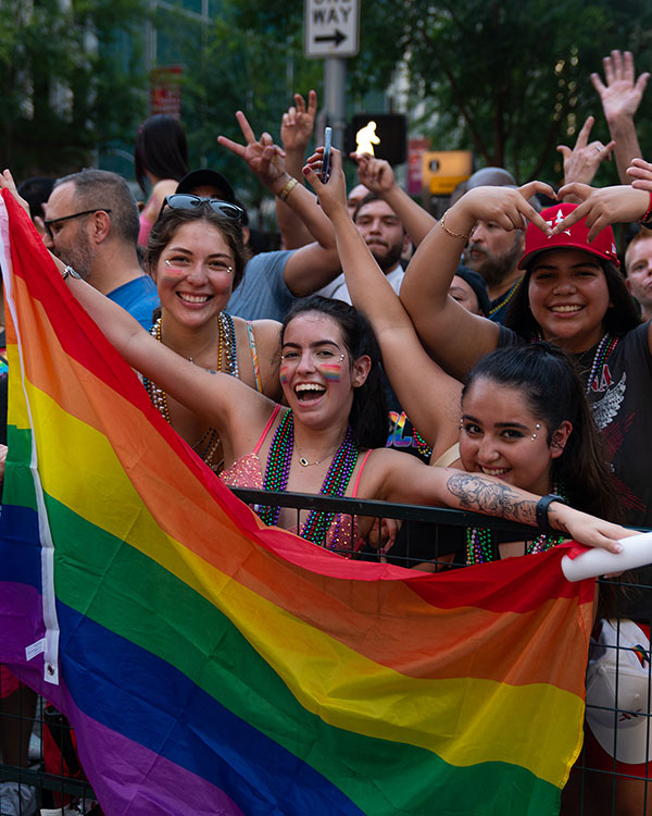 Parade watchers at the Houston Pride Parade hold a Pride flag open and smile for the picture.