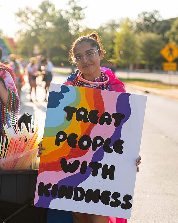 A Rice student holds up a sign they brought to hold in the parade that says "Treat people with kindness."