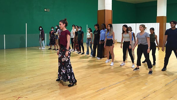 Inside of a room that looks like a dance studio the flamenco instructor stands in front of a group of Rice students showing them how to dance.