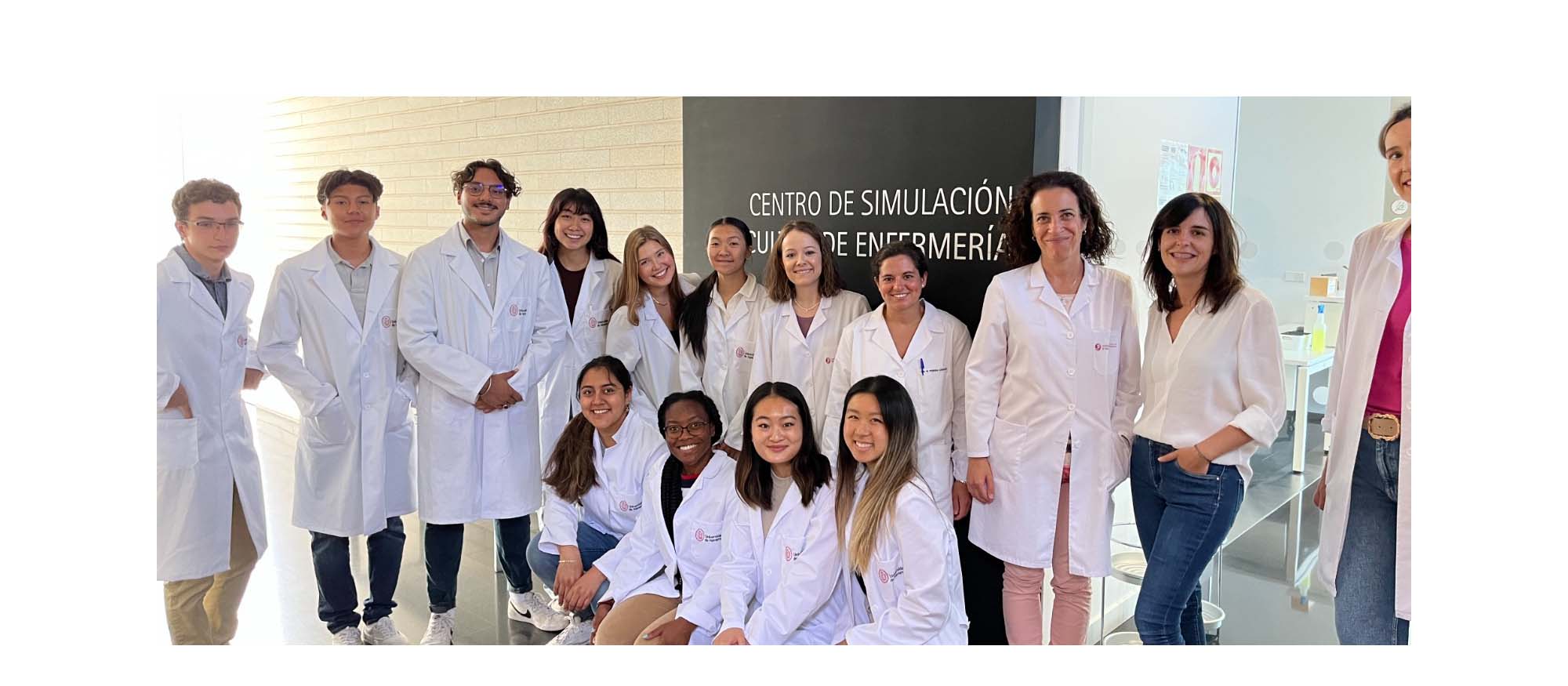 A group of Rice students wearing white lab coats smile and pose for a picture with their professors.