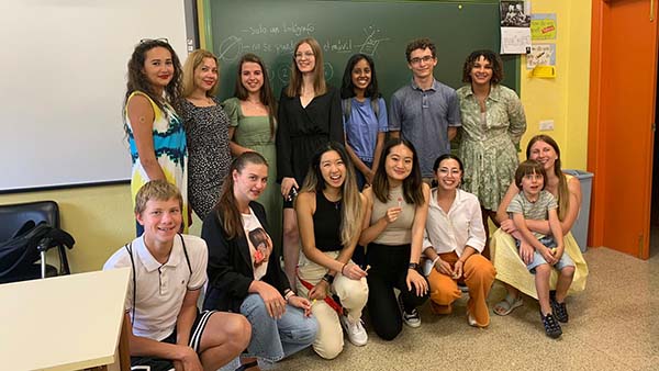 Linda poses for a group picture in front of a chalkboard inside of a classroom alongside the students she taught and her fellow peer-teachers.