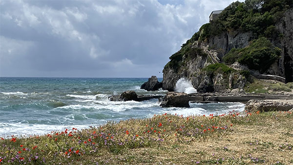 A scenery picture of the coast of Cosa, Italy, featuring a large cliffside and some water.