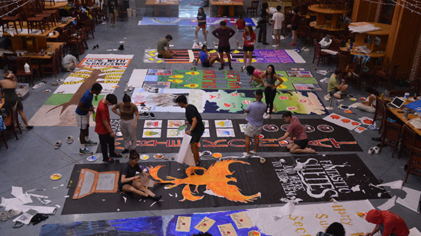 A photo taken from above of a group of students working on very large banners laid out all over the floor.