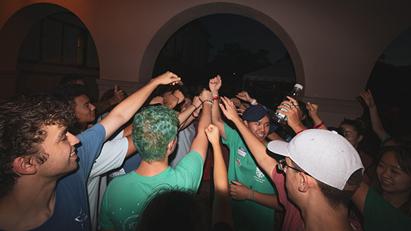A group of students stands in a circle with their hands up, meeting in the middle like a huddle.