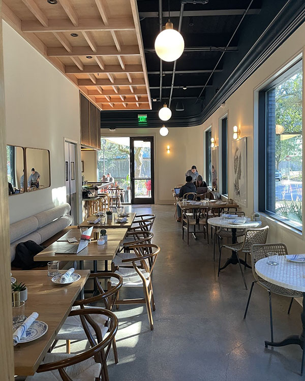 A picture of empty tables and chairs on either side of a mid-sized hallway inside of a Houston coffee shop.