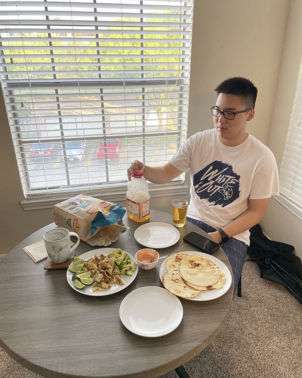 A picture of a Rice student, John, sitting at a table with plates of ingredients in front of him to make fish tacos.