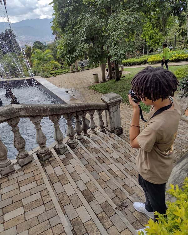 The picture shows the side profile of Arinze, a Rice student, as he takes a picture of a fountain in front of him.