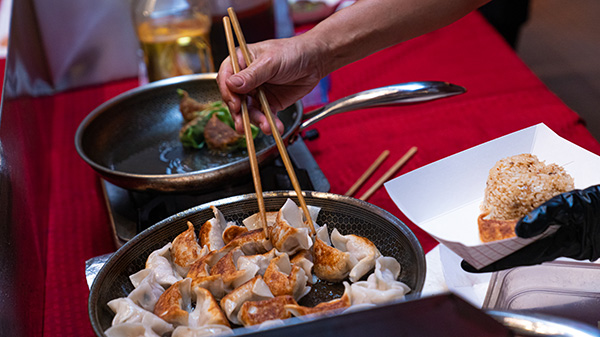 A close up shot of a cook frying dumplings with chopsticks in a large pan. 