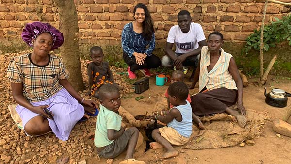 Puneetha sitting with a Ugandan family watching four kids play on the ground.