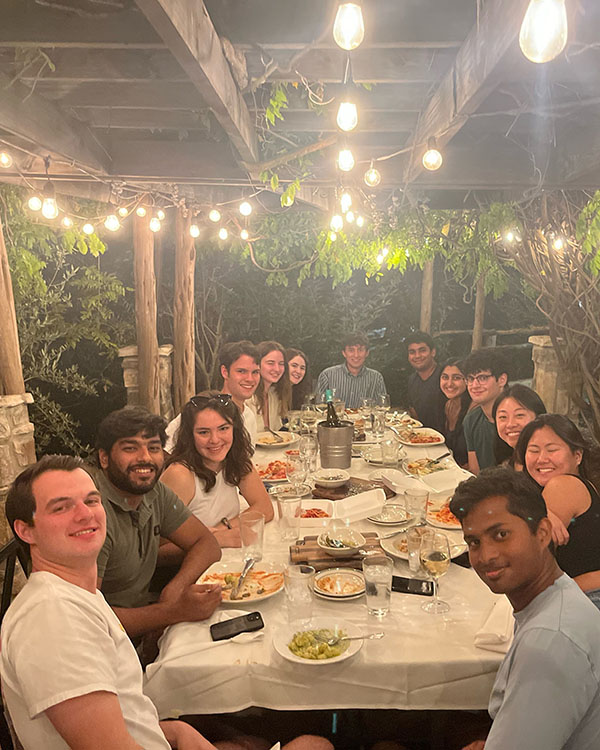Picture taken from the head of a long dinner table with students sitting on both sides with plates of food in front of them.
