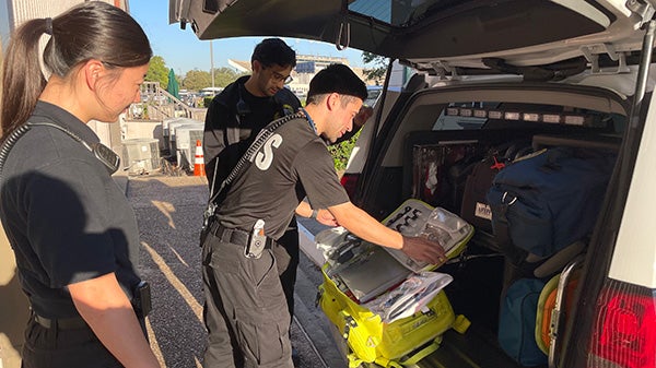 A group of Rice students wearing clothes that identify them as emergency services lean over the back of a trunk filled with gear for rendering emergency care.