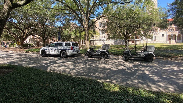 A picture of a large white suburban that says EMS parked on the side of Rice inner loop street, and behind it are two empty golf carts that also say EMS on the side.