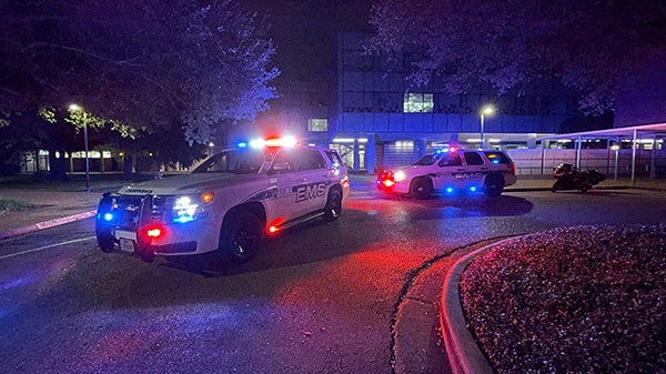 A picture taken at night time of two large white suburbans parked on a street with their blue and red emergency lights on.