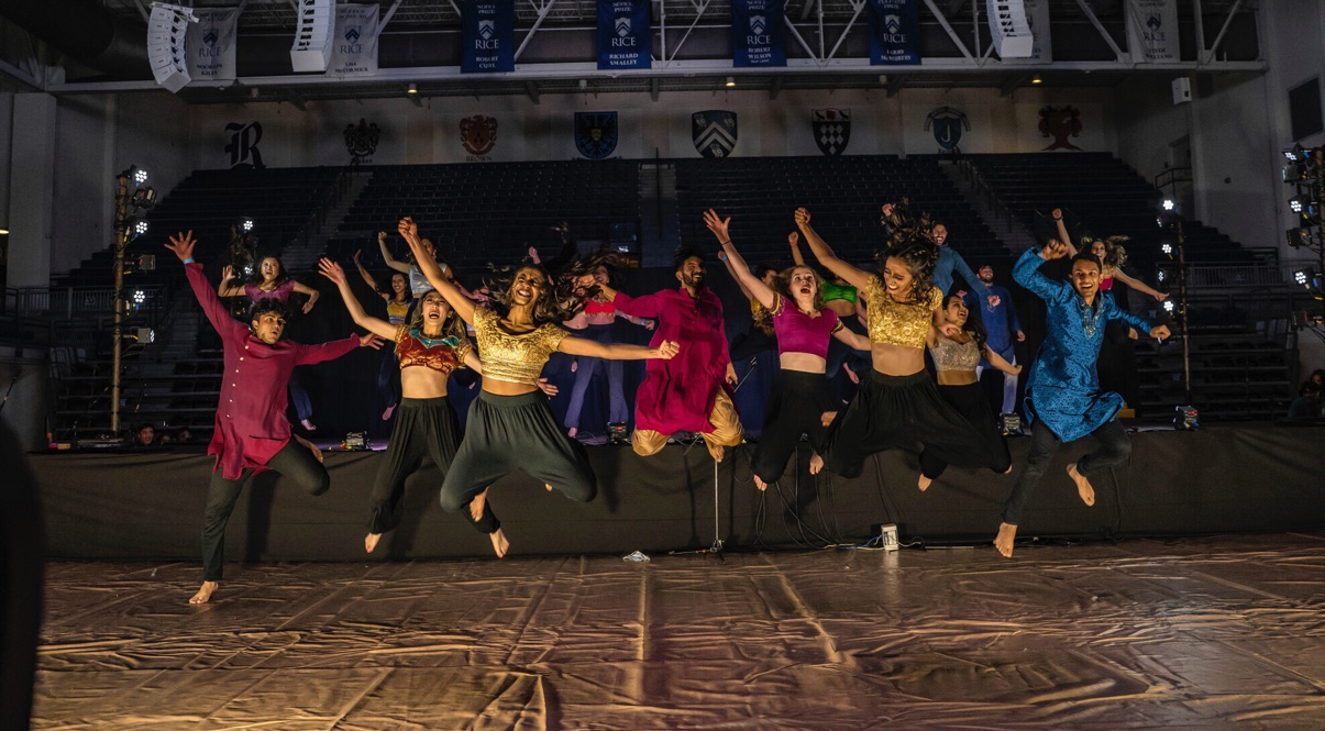 Several students in a jumping pose wearing traditional south asian outfits.
