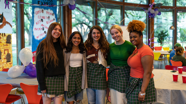 Five students standing next to each other in a single row, wearing kilts and smiling.