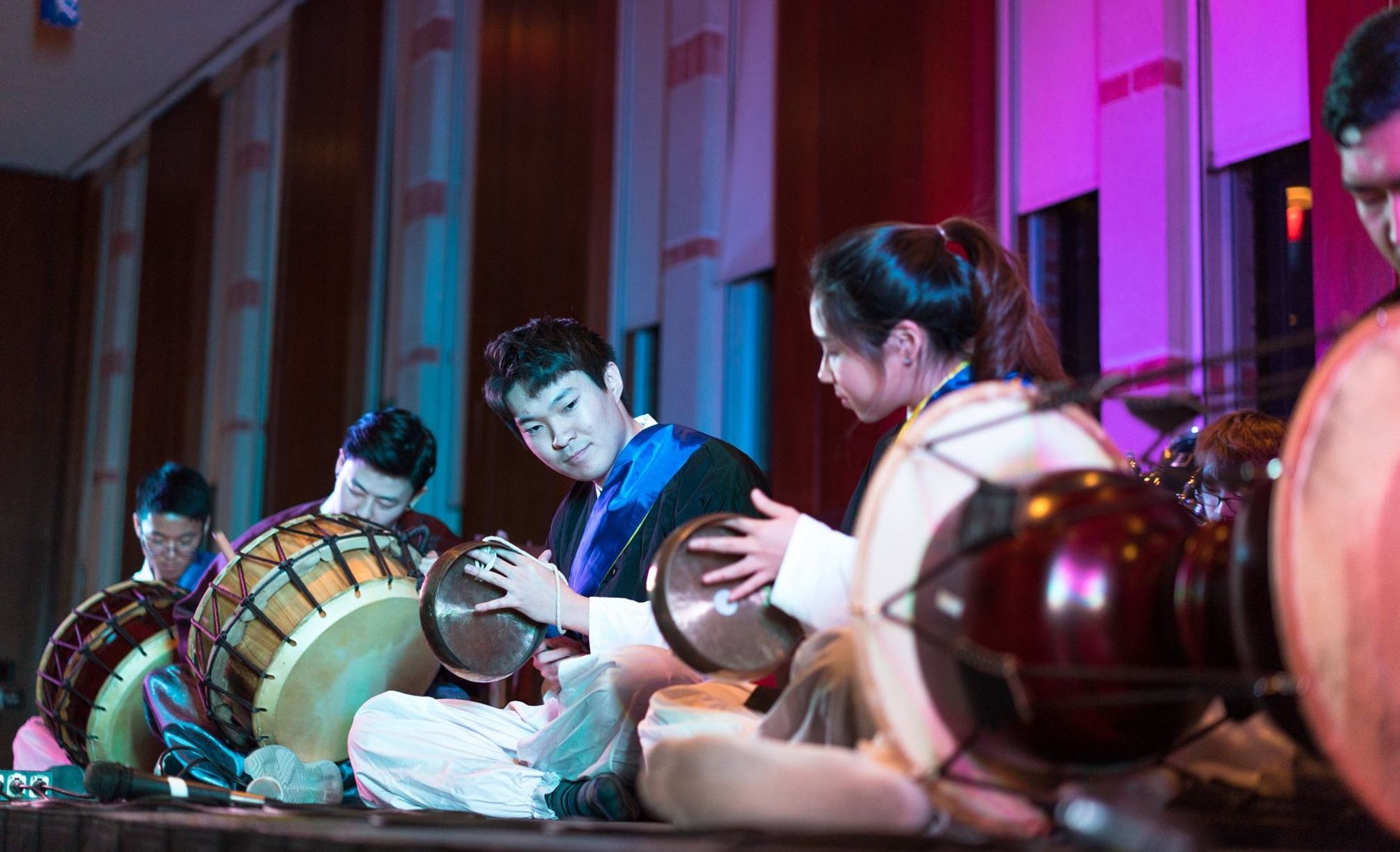 Five students sitting on a stage playing traditional Korean drums.
