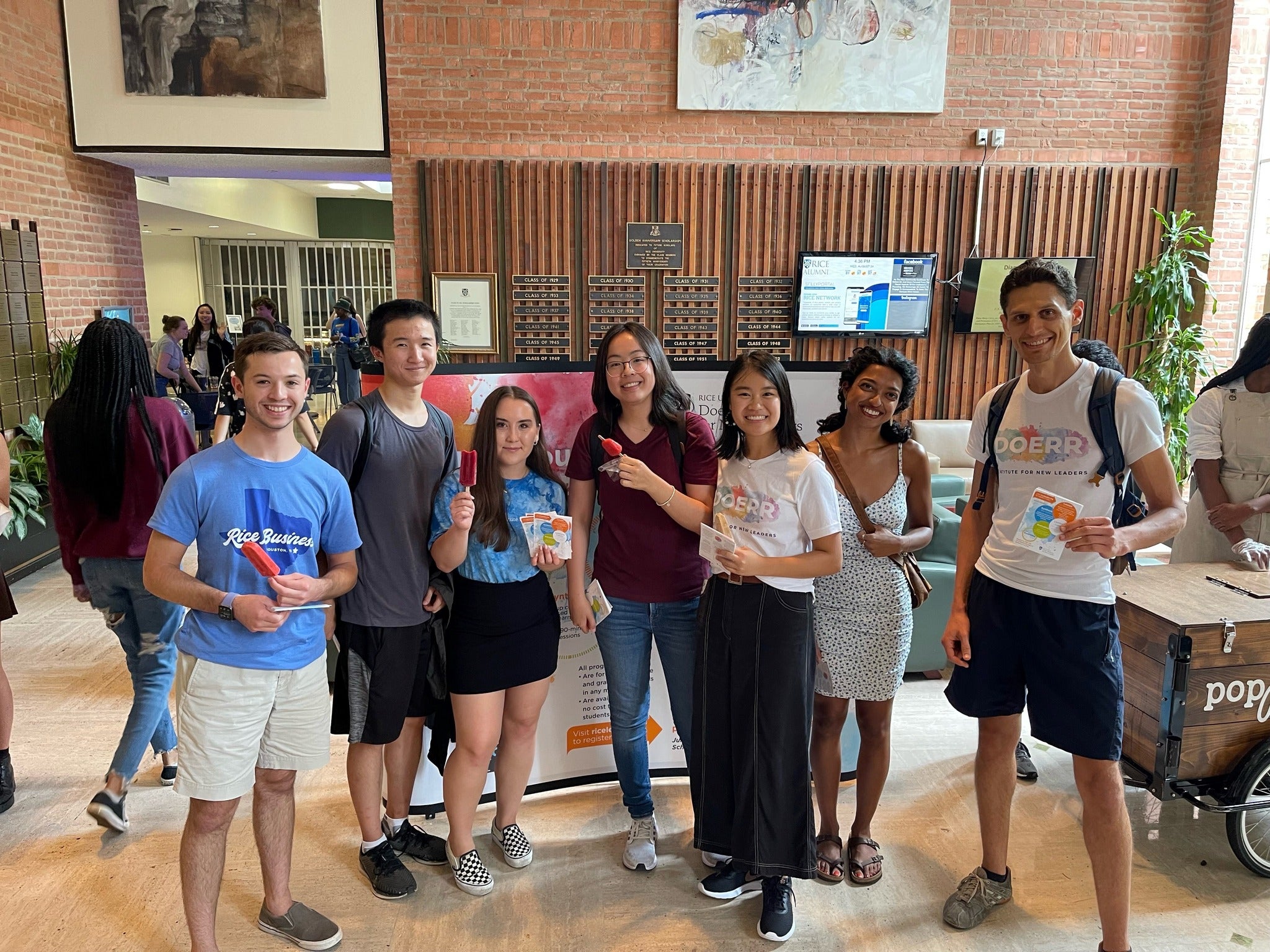 A group of students standing in a row, holding red popsicles and flyers while smiling at the camera.