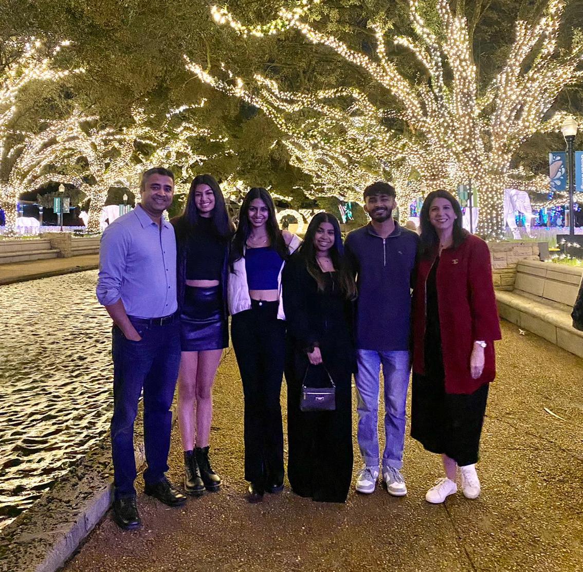 A group photo with 6 people and a trail of trees decorated with white lights in the background.
