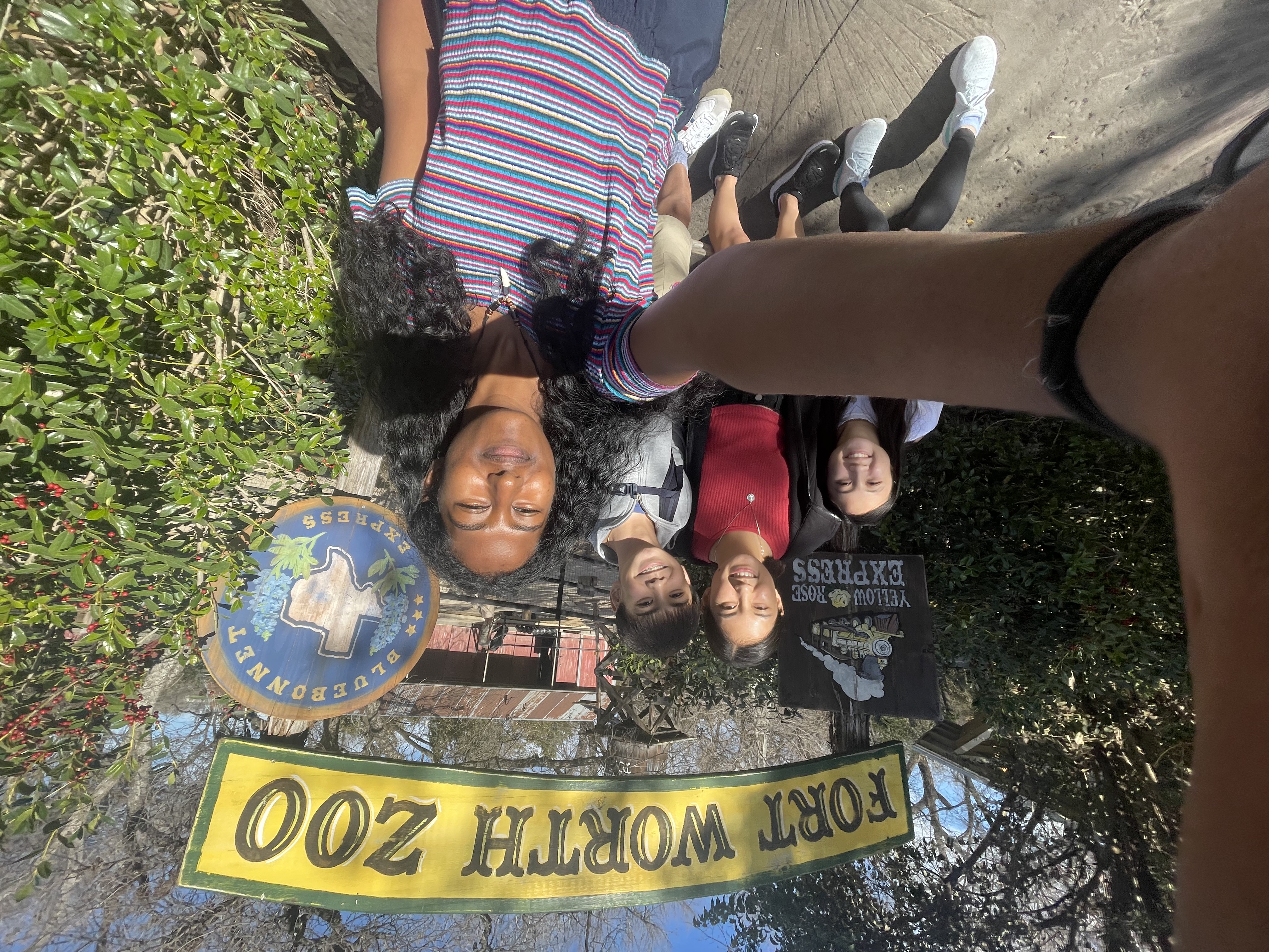 A selfie taken by one person with four people in frame and a "Fort Worth Zoo" sign behind them.