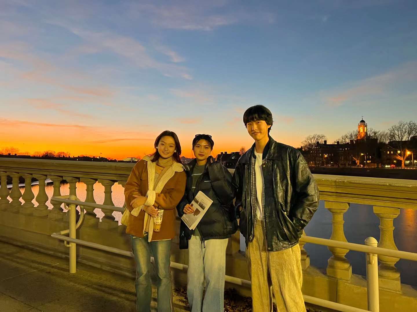 A picture of three students standing on a bridge with a nice sunset behind them.