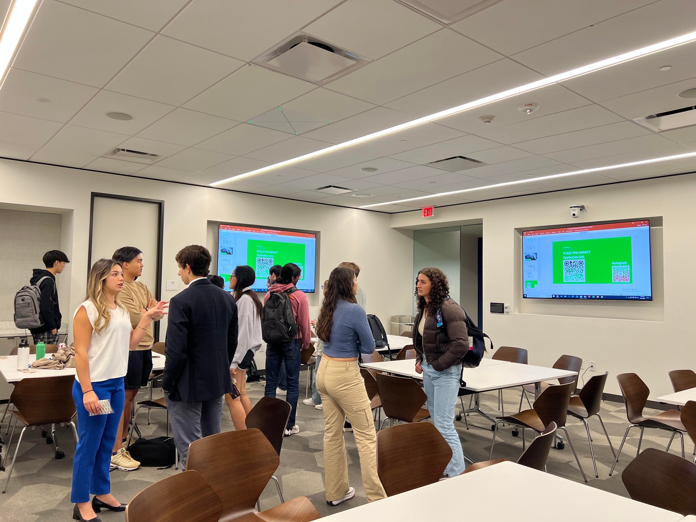 Students standing in a classroom talking to one another.